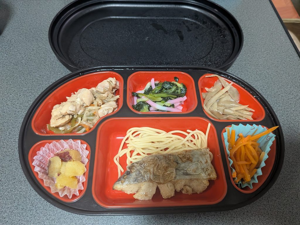 コープデリの宅食で届いた肉料理やスパゲッティ、野菜のおかずが入った夕食弁当